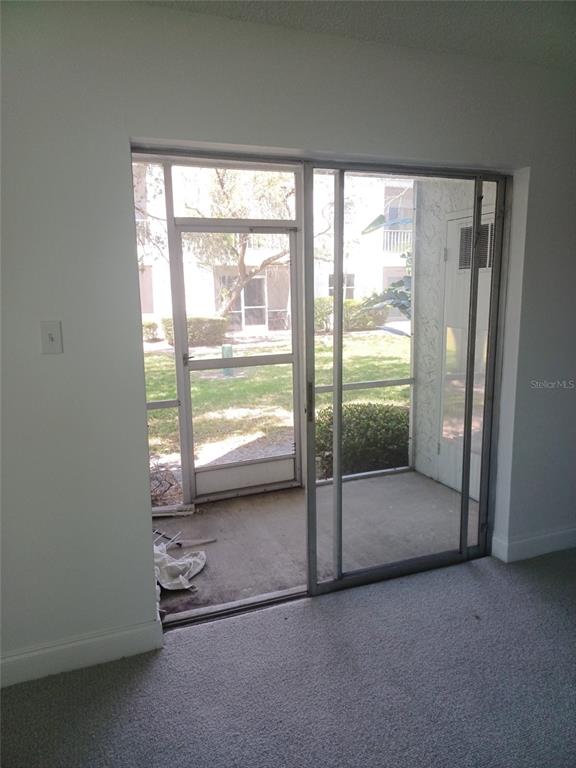 A room with gray carpet features a sliding glass door opening to a screened patio — 245 S MCMULLEN BOOTH ROAD UNIT 17, CLEARWATER, FL