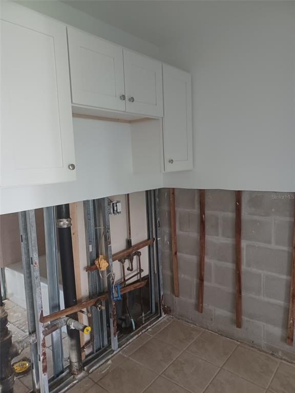 An unfinished room features exposed wall studs, plumbing pipes, and white upper kitchen cabinets — 245 S MCMULLEN BOOTH ROAD UNIT 17, CLEARWATER, FL
