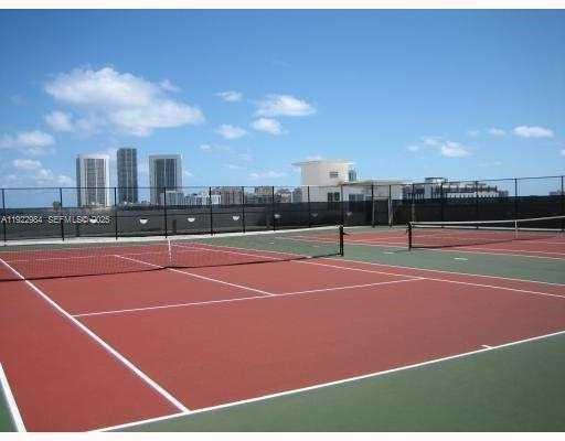 An outdoor tennis court with a red surface and a black chain-link fence — 1755 E Hallandale Beach Blvd # 1005E, Hallandale Beach FL 33009, HALLANDALE BEACH, FL