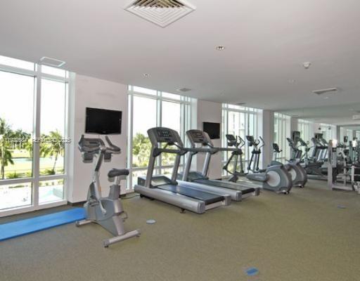 A bright fitness center features several treadmills, stationary bikes, and large windows overlooking palm trees — 1755 E Hallandale Beach Blvd # 1005E, Hallandale Beach FL 33009, HALLANDALE BEACH, FL