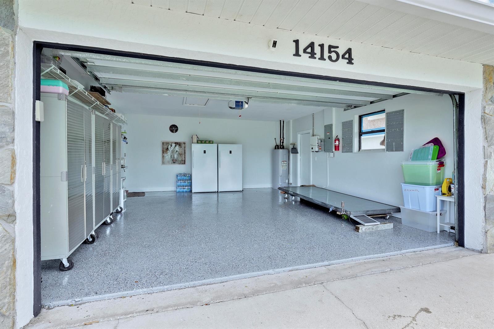 A clean, two-car garage features a speckled epoxy floor, white walls, and storage cabinets — 14154 Aster Avenue, Wellington FL 33414, WELLINGTON, FL