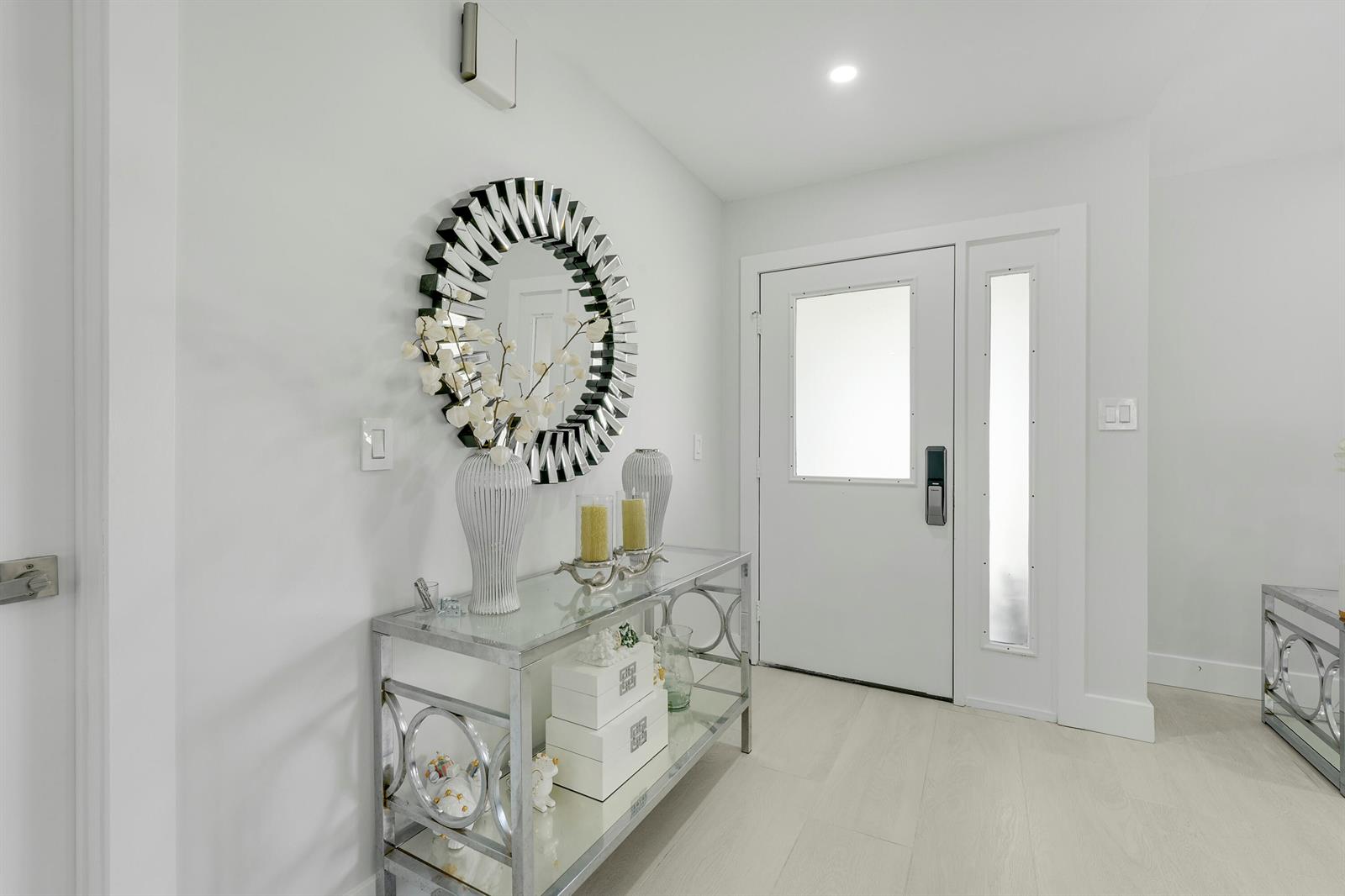 A bright entryway features a glass console table, a circular mirror, and a white door — 14154 Aster Avenue, Wellington FL 33414, WELLINGTON, FL