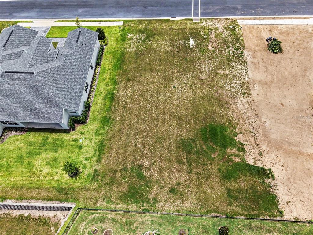 An aerial view shows a vacant residential lot situated between a house and an empty plot — 212 SNOWY ORCHID WAY, LAKE ALFRED, FL