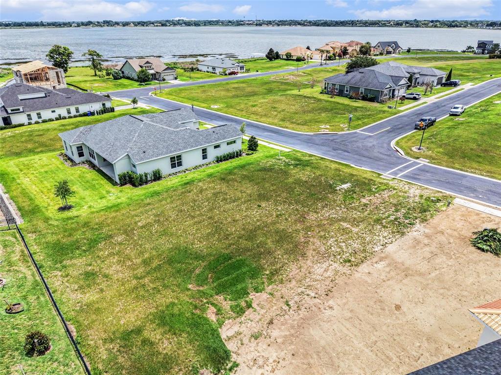 An aerial view shows a vacant residential lot next to a house near a lake — 212 SNOWY ORCHID WAY, LAKE ALFRED, FL