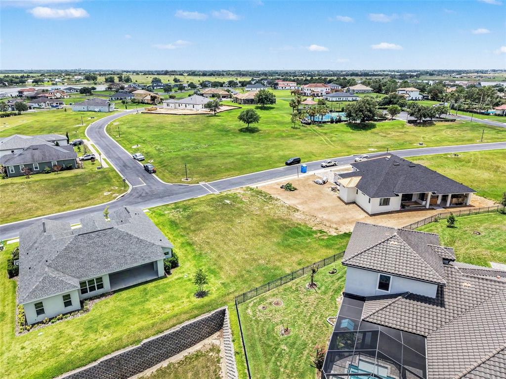 An aerial view shows several suburban houses, paved roads, and open green fields — 212 SNOWY ORCHID WAY, LAKE ALFRED, FL