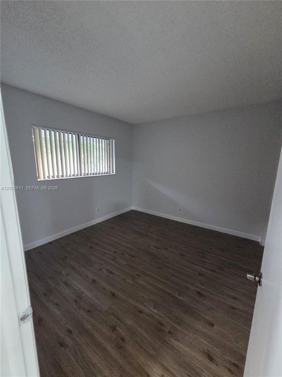 An empty bedroom features light gray walls, white trim, and dark wood-look flooring — 1170 NW 80th Ave # 203, Margate FL 33063, MARGATE, FL