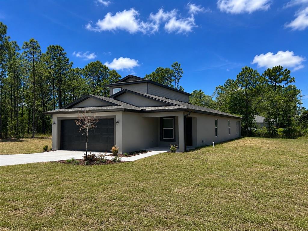 A single-story house with a dark garage door and light exterior walls sits on a lawn — 15197 DUCK HAWK ROAD, BROOKSVILLE, FL