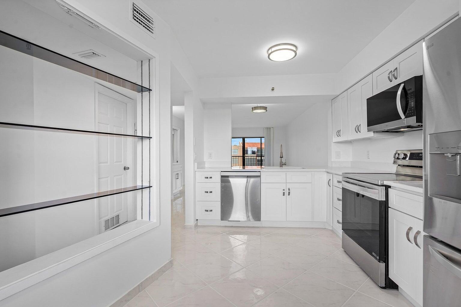 A white kitchen features stainless steel appliances, tile flooring, and an open pass-through window — 14475 Strathmore Lane # 707, Delray Beach FL 33446, DELRAY BEACH, FL