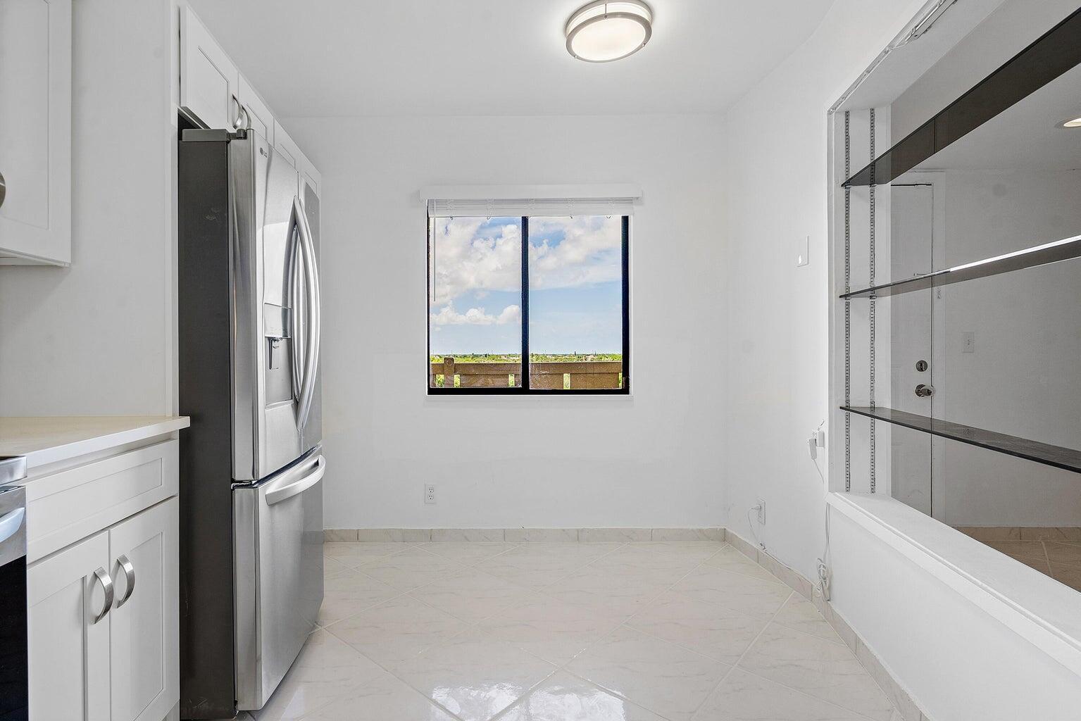 A kitchen dining area features a stainless steel refrigerator, white cabinets, and glass shelving — 14475 Strathmore Lane # 707, Delray Beach FL 33446, DELRAY BEACH, FL