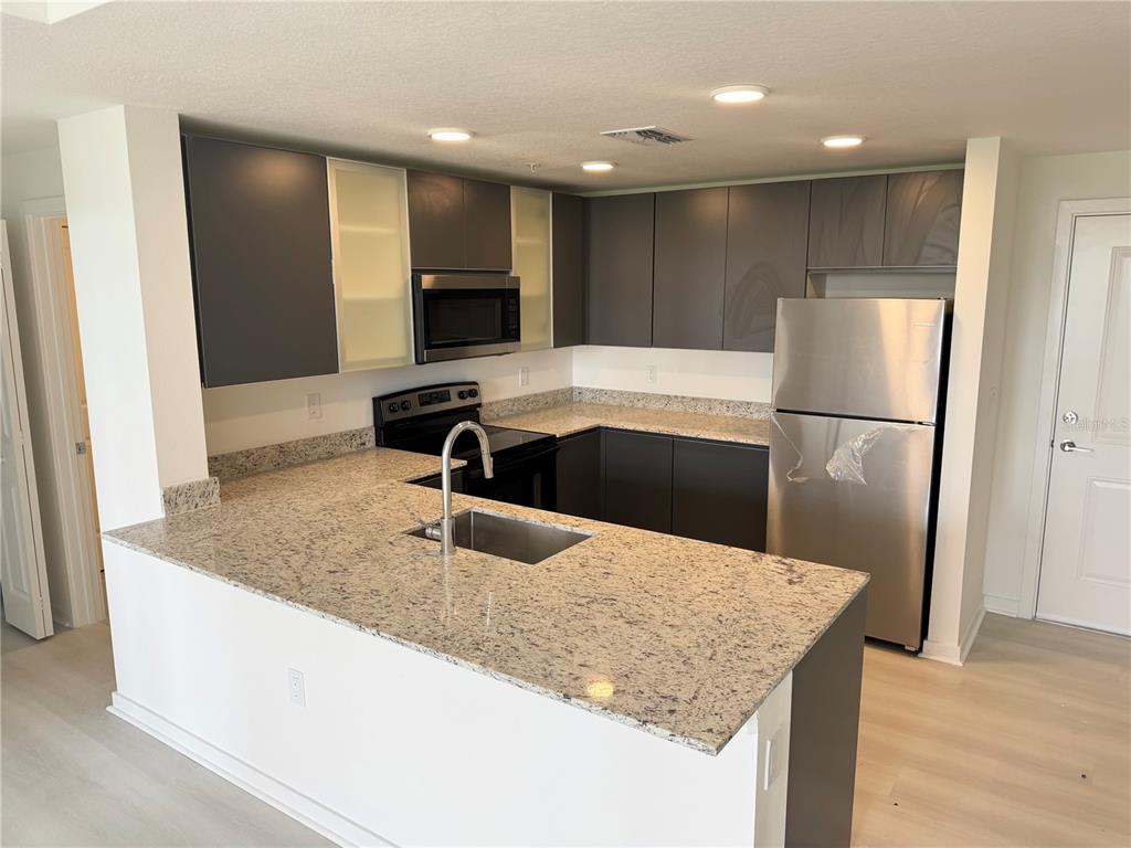 A kitchen features dark gray cabinets, granite countertops, stainless steel appliances, and a breakfast bar — 5579 MILLENIA PARK BOULEVARD UNIT 322, ORLANDO, FL
