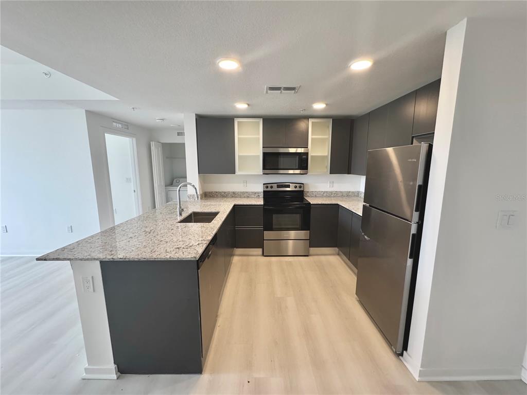 A modern kitchen features dark gray cabinetry, stainless steel appliances, and light granite countertops — 5579 MILLENIA PARK BOULEVARD UNIT 322, ORLANDO, FL