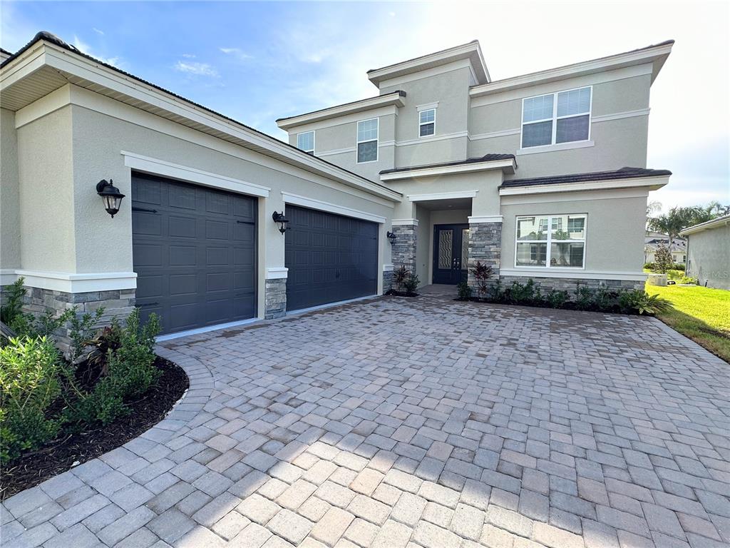 A two-story house features a paved driveway, a three-car garage, and stone veneer accents — 3392 ACACIA BAY AVENUE, WESLEY CHAPEL, FL