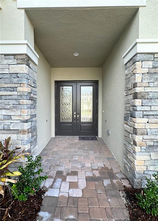 A covered entryway features double front doors, stone pillars, and a paver walkway — 3392 ACACIA BAY AVENUE, WESLEY CHAPEL, FL