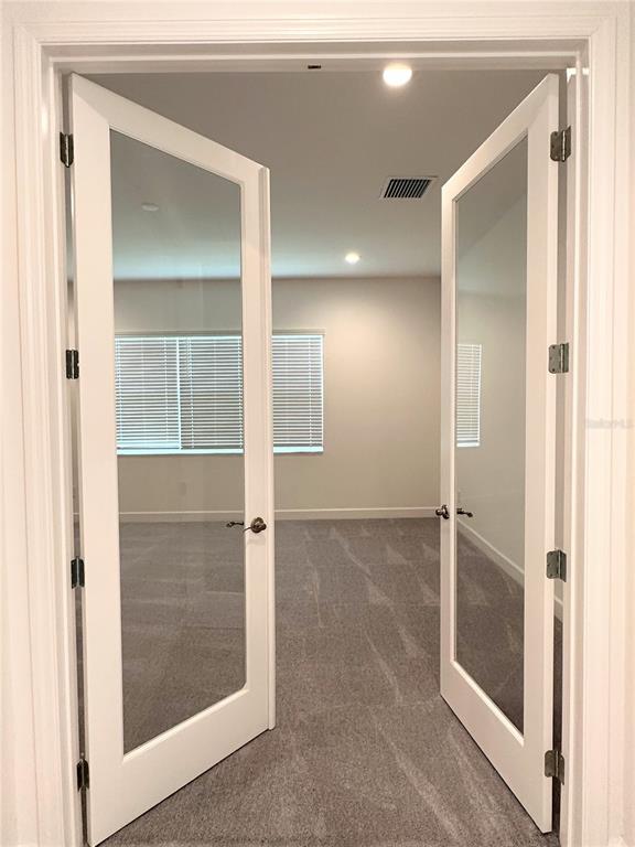 A view through open French doors into a carpeted room with a window and blinds — 3392 ACACIA BAY AVENUE, WESLEY CHAPEL, FL
