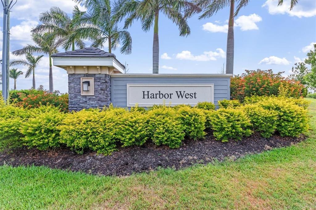 A stone and wood monument sign for Harbor West stands surrounded by landscaping and palms — 15153 SPANISH POINT DRIVE, PORT CHARLOTTE, FL