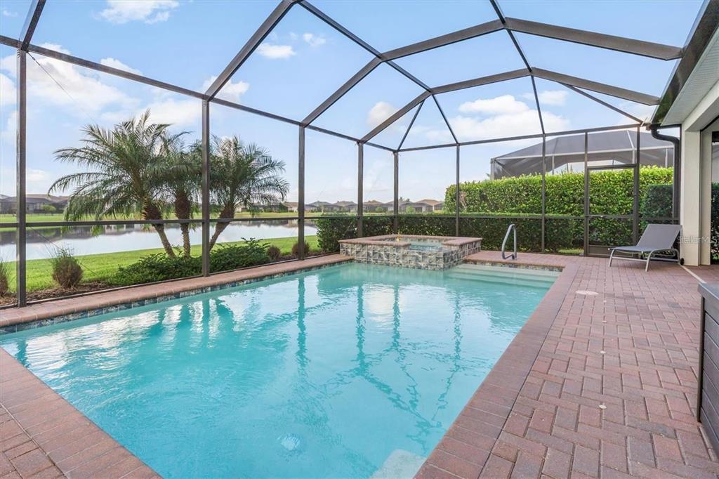 A screened-in swimming pool and spa with a brick paver deck overlooking a lake — 15153 SPANISH POINT DRIVE, PORT CHARLOTTE, FL