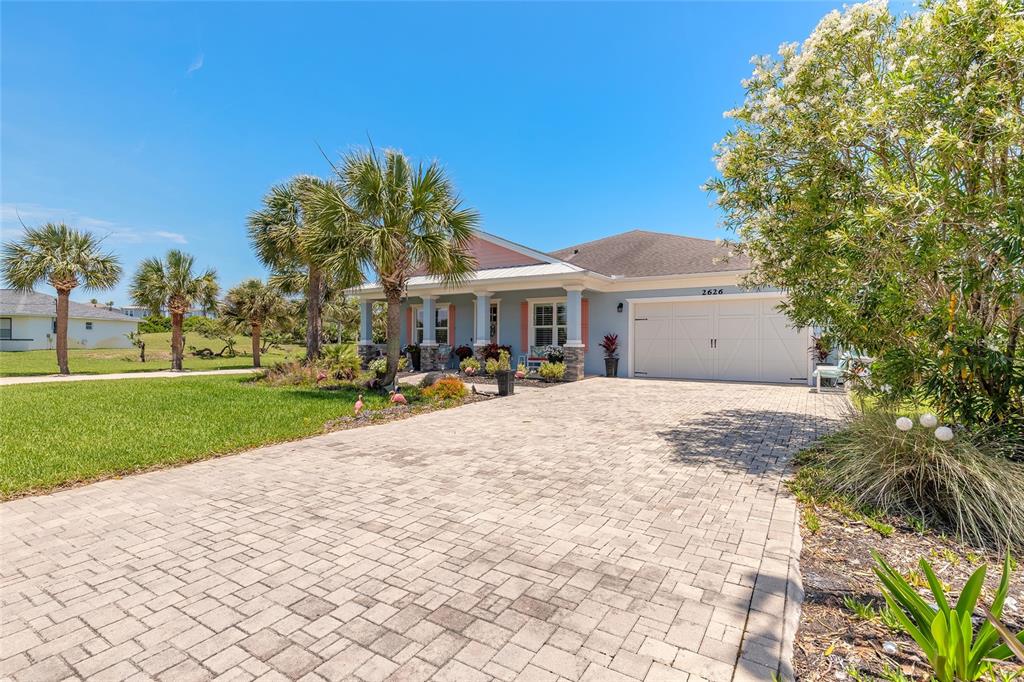 A light blue house with a paver driveway and palm trees under a clear sky — 2626 OSPREY CIRCLE N, FLAGLER BEACH, FL
