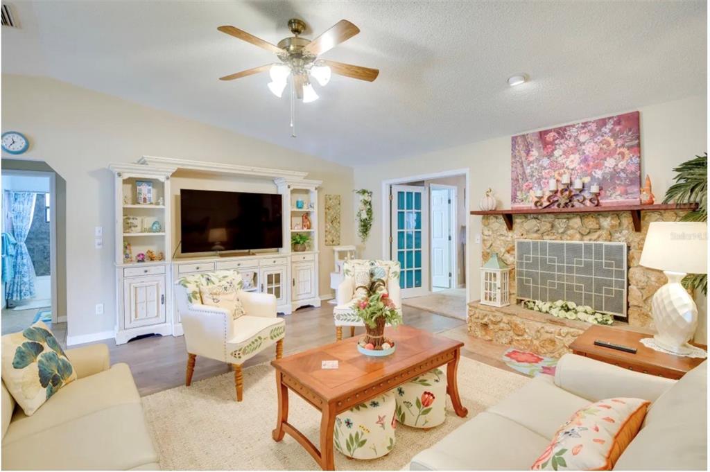A living room features a stone fireplace, a large television unit, and a ceiling fan — 2737 FERN PALM DRIVE, EDGEWATER, FL