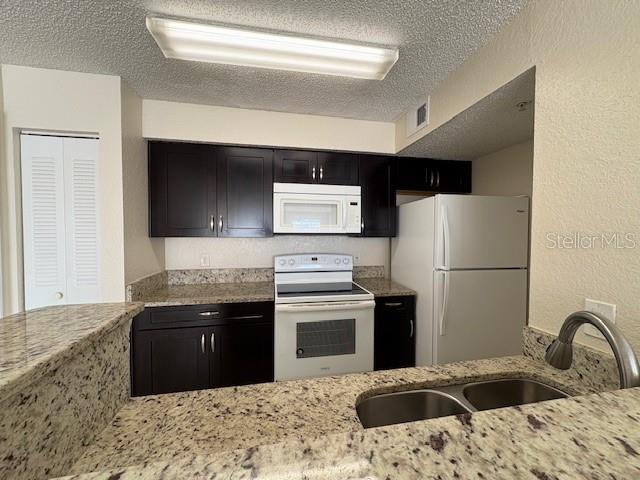 A kitchen features dark cabinets, granite countertops, white appliances, and a double-basin sink — 2210 GRAND CAYMAN COURT UNIT 1722, KISSIMMEE, FL
