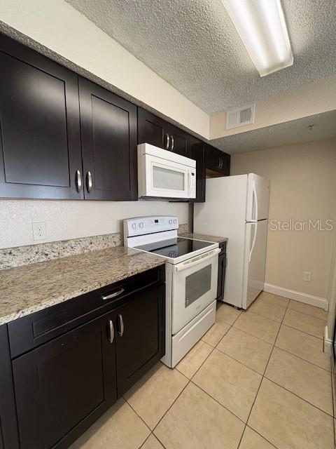 A kitchen features dark wood cabinets, granite countertops, white appliances, and light-colored tile flooring — 2210 GRAND CAYMAN COURT UNIT 1722, KISSIMMEE, FL