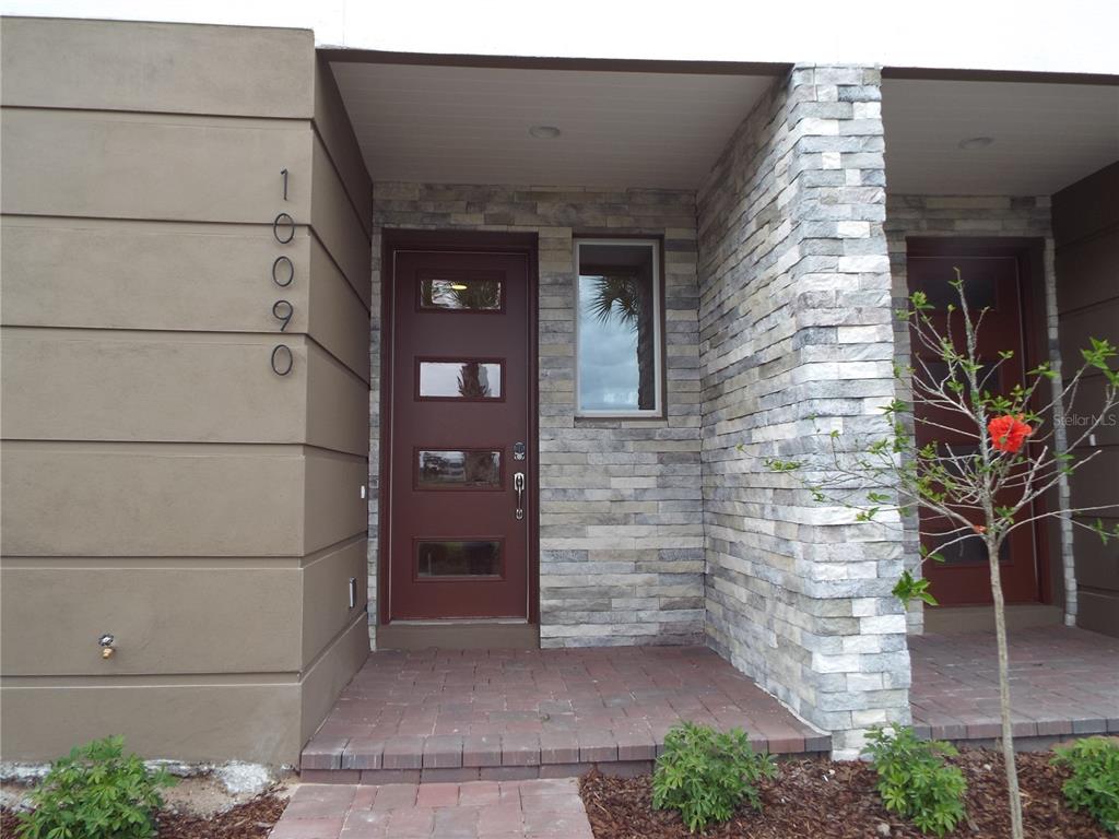 A modern home entrance features a brown door, stone veneer siding, and brick pavers — 10090 SUNNIFA ALLEY, ORLANDO, FL