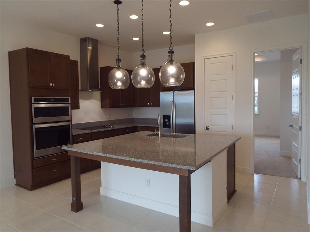 A kitchen features dark wood cabinets, stainless steel appliances, a granite island, and pendant lighting — 10090 SUNNIFA ALLEY, ORLANDO, FL