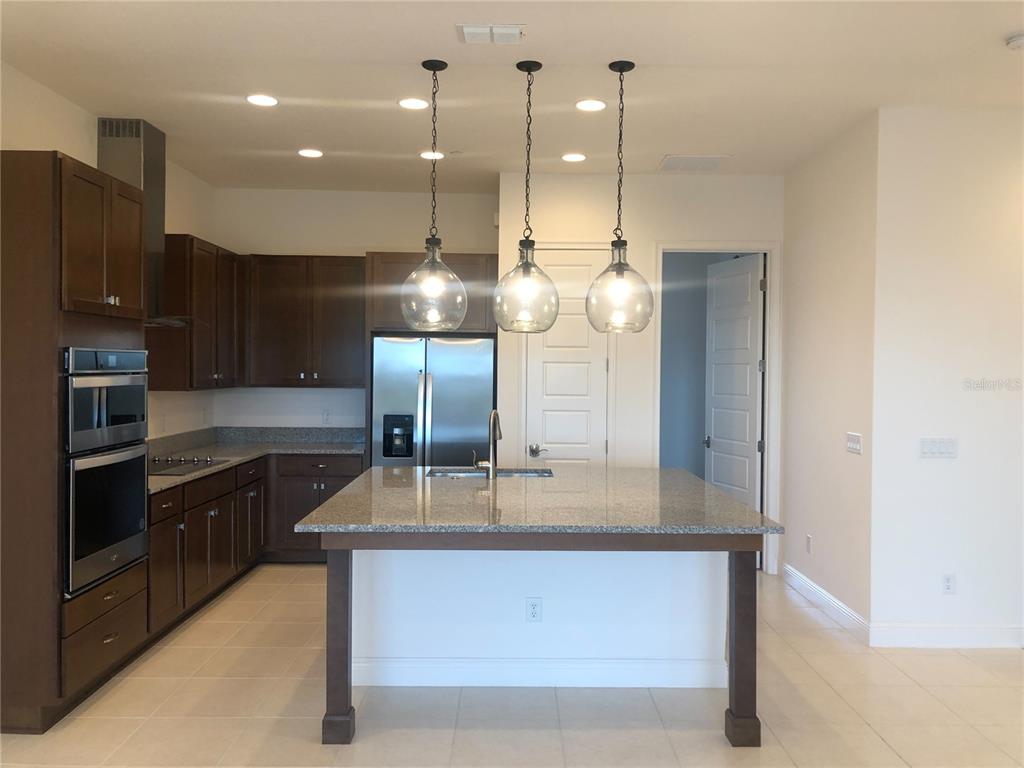 A kitchen features dark wood cabinets, granite countertops, a central island, and three pendant lights — 10090 SUNNIFA ALLEY, ORLANDO, FL