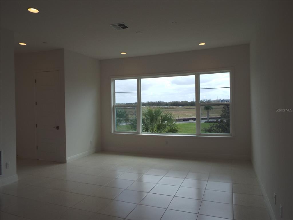 An empty room with white tile floors, recessed lighting, and a large window overlooking fields — 10090 SUNNIFA ALLEY, ORLANDO, FL