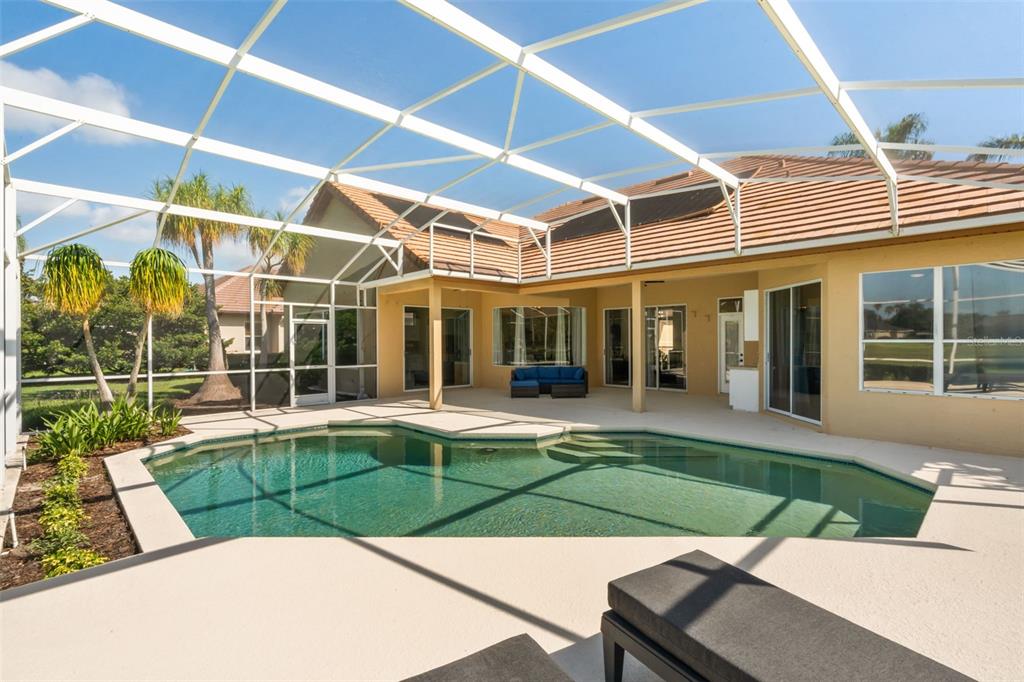 A swimming pool with a screened enclosure sits on a patio behind a tan house — 11217 WILLOW GARDENS DRIVE, WINDERMERE, FL