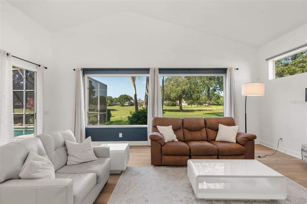 A living room features a white sofa, brown leather sofa, and large windows overlooking greenery — 11217 WILLOW GARDENS DRIVE, WINDERMERE, FL