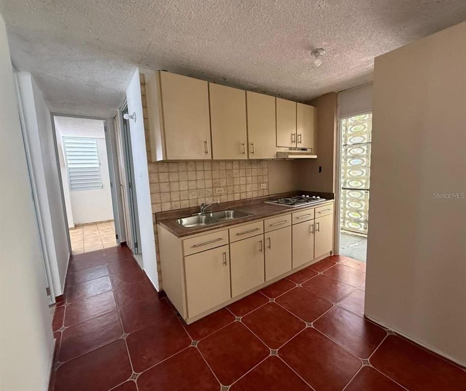A kitchen features beige cabinets, a tiled backsplash, and reddish-brown floor tiles — Condominio Terrazul CONDOMINIO TERRAZUL UNIT 2/1, ARECIBO, PR
