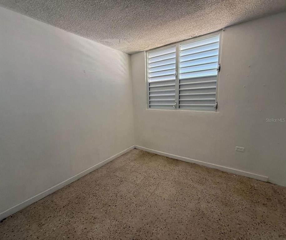 An empty bedroom features white walls, a textured ceiling, a louvered window, and terrazzo flooring — Condominio Terrazul CONDOMINIO TERRAZUL UNIT 2/1, ARECIBO, PR