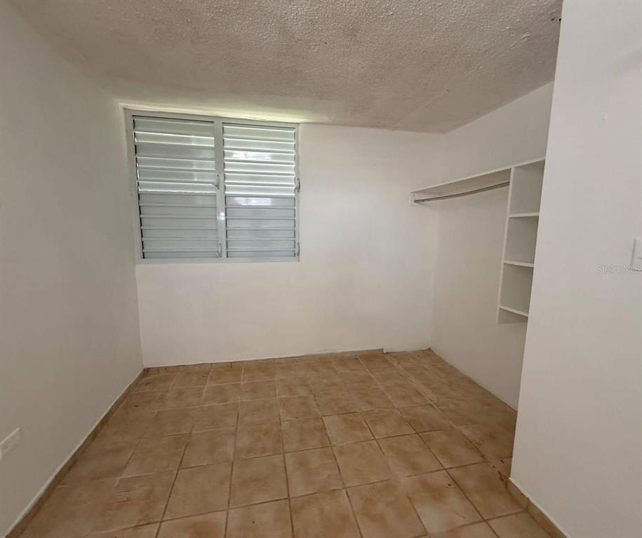 An empty bedroom features white walls, a louvered window, tile flooring, and built-in closet shelving — Condominio Terrazul CONDOMINIO TERRAZUL UNIT 2/1, ARECIBO, PR