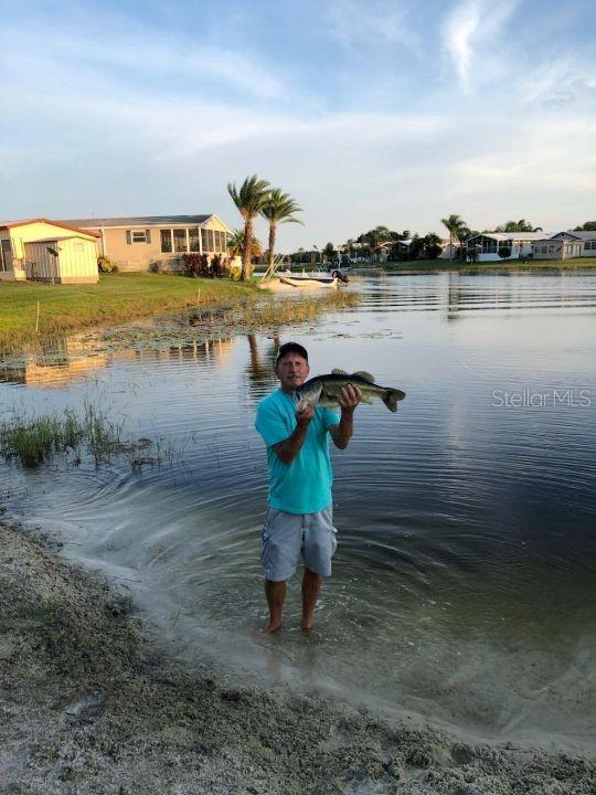 A man stands in a lake holding a large fish in front of waterfront homes — 21 SILVERSIDES STREET, LAKE WALES, FL