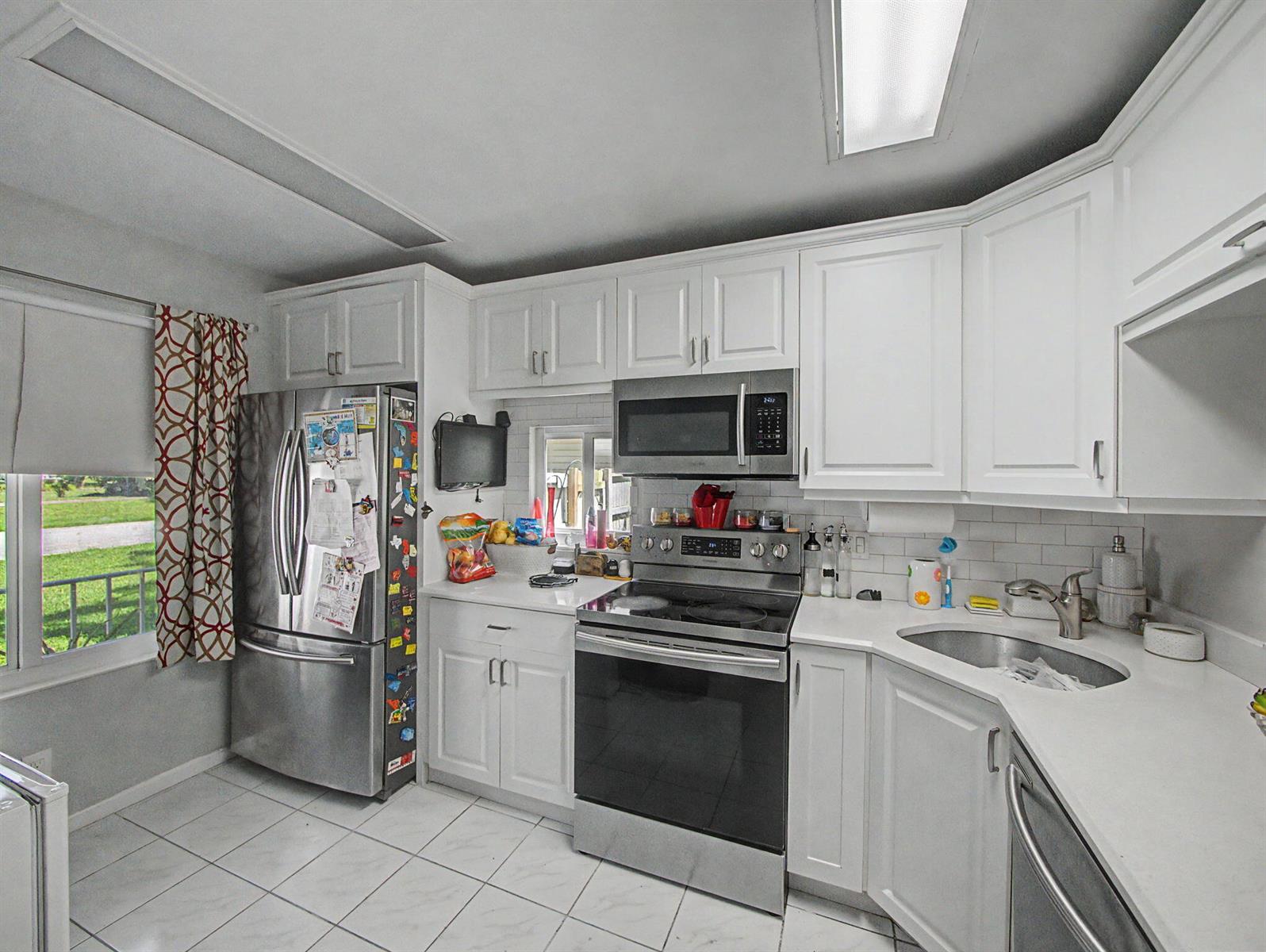 A kitchen features white cabinets, stainless steel appliances, a corner sink, and tiled flooring — 4675 Lakeside Circle, West Palm Beach FL 33417, WEST PALM BEACH, FL