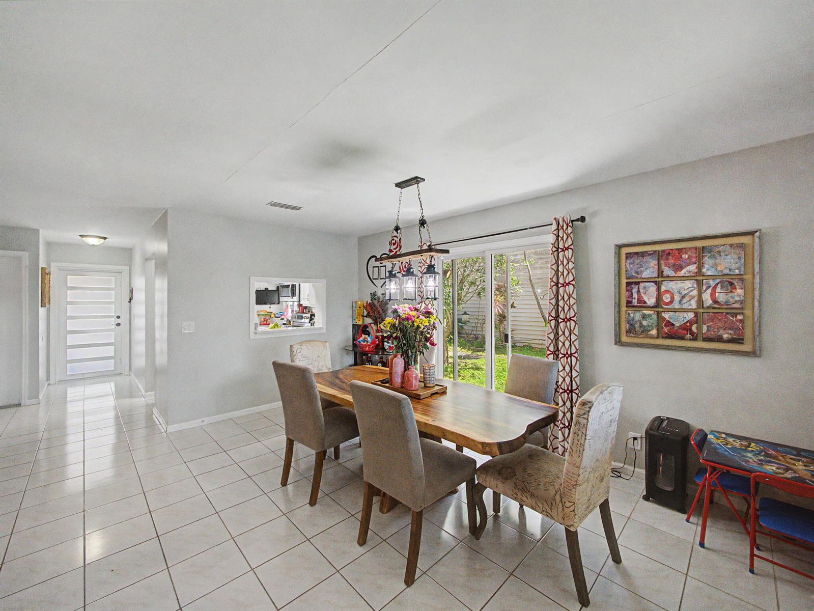 A dining room features a wooden table, upholstered chairs, a chandelier, and a sliding glass door — 4675 Lakeside Circle, West Palm Beach FL 33417, WEST PALM BEACH, FL