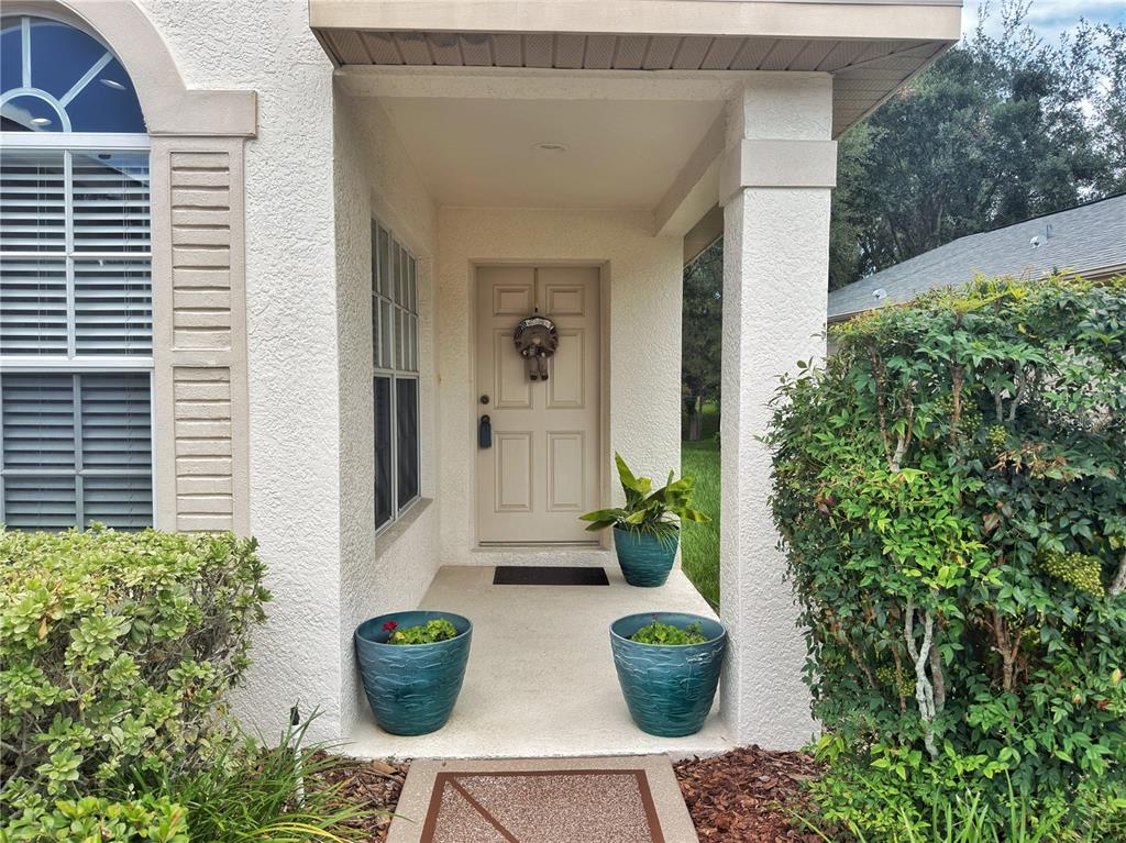 The exterior entrance features a beige door, a covered porch, and three potted plants — 259 CENTER OAK CIRCLE, SPRING HILL, FL