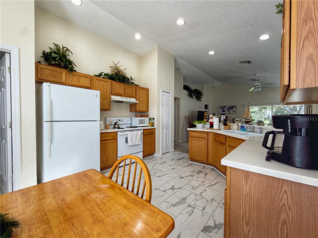 A kitchen features oak cabinets, white appliances, a breakfast table, and white marble-patterned tile flooring — 259 CENTER OAK CIRCLE, SPRING HILL, FL