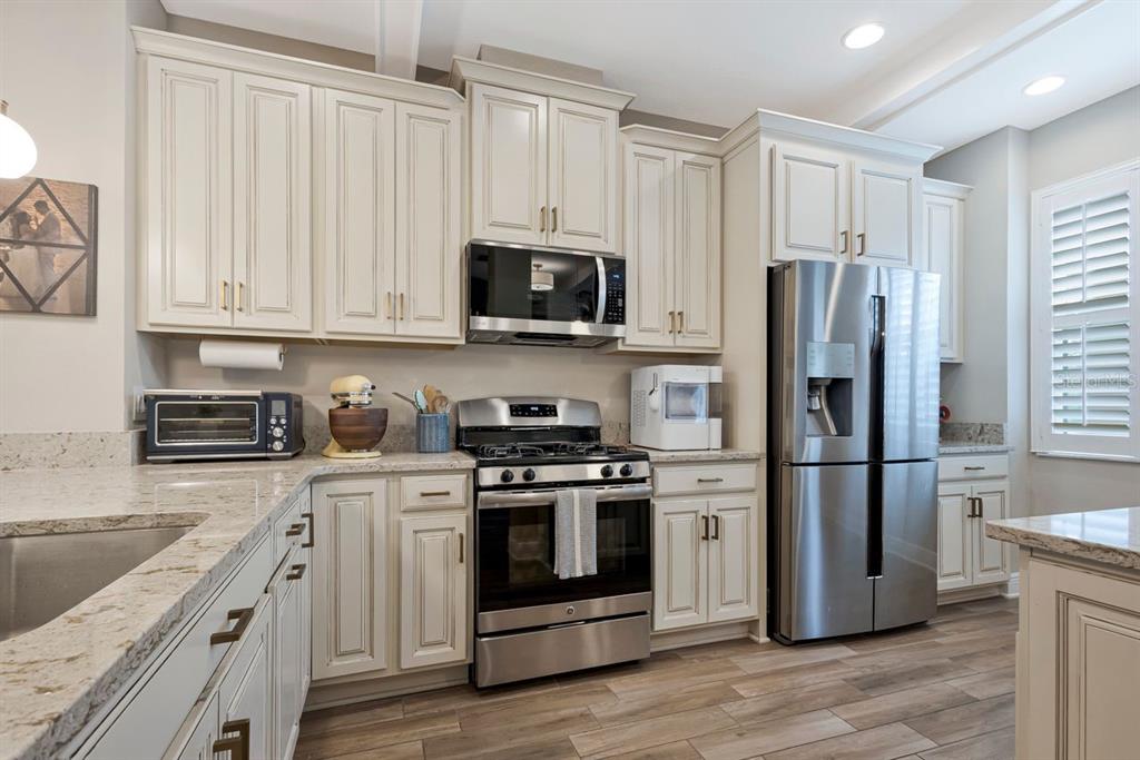 A kitchen features cream-colored cabinets, stainless steel appliances, and light granite countertops — 13027 BATTEN LANE, ODESSA, FL