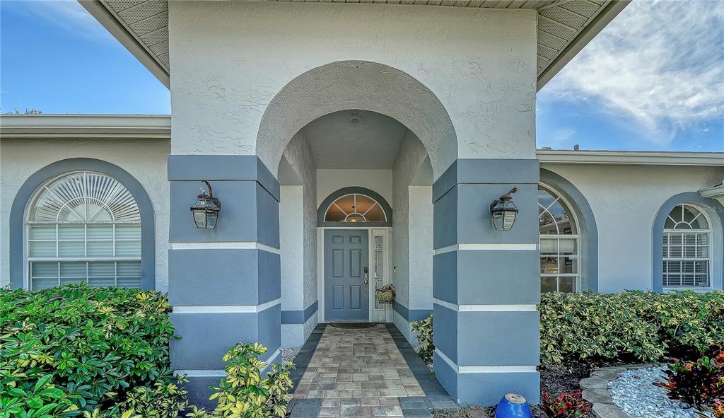 A front entryway features a covered arched porch, a blue door, and two exterior lanterns — 9528 HAWKSMOOR LANE, SARASOTA, FL