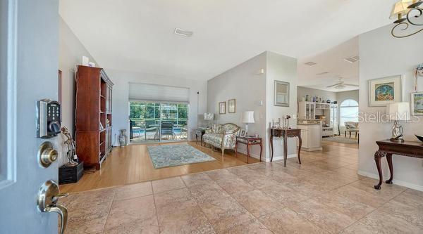 An entryway with tile flooring opens into a living room featuring hardwood floors and furniture — 9528 HAWKSMOOR LANE, SARASOTA, FL