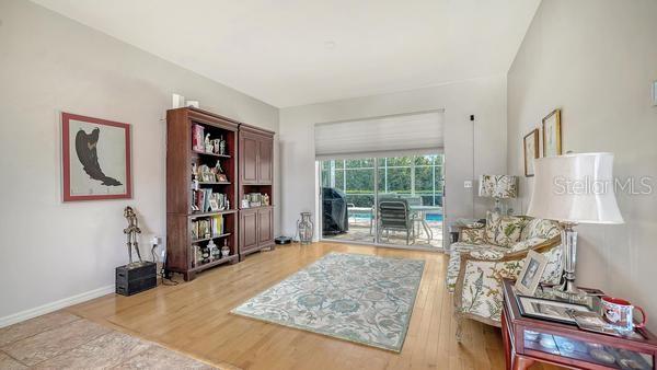 A living room with hardwood floors, a large wooden bookshelf, and a sliding glass door — 9528 HAWKSMOOR LANE, SARASOTA, FL