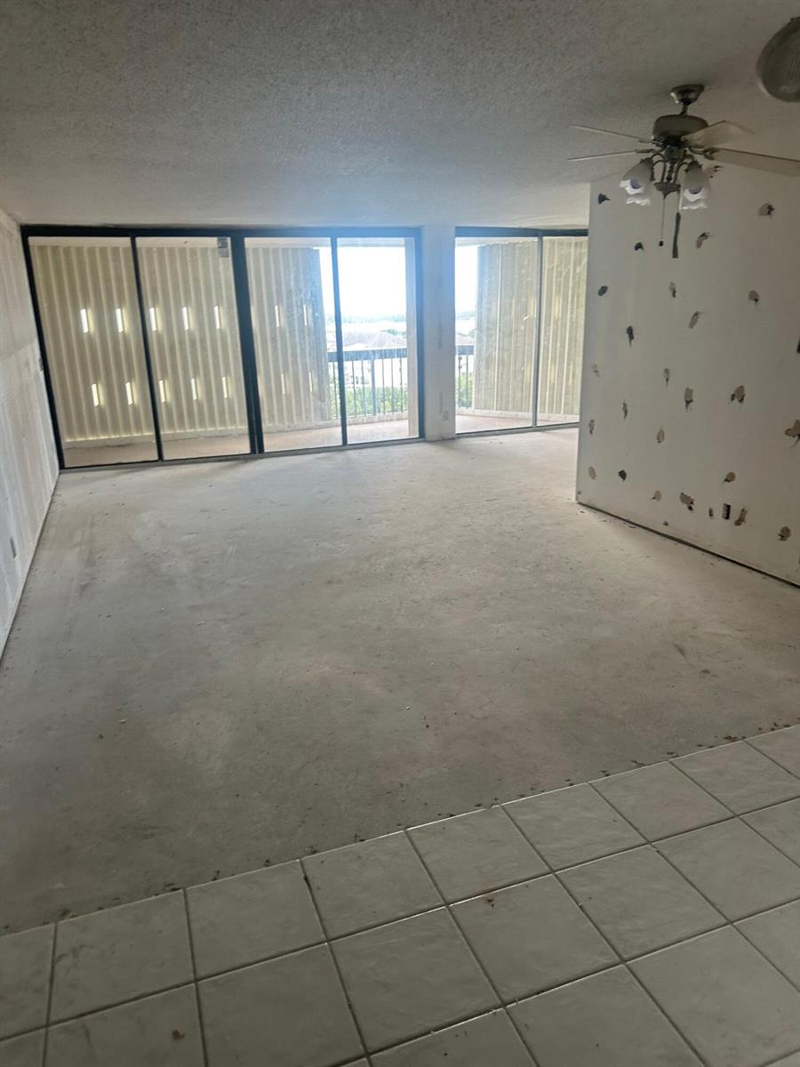 An unfinished living room with concrete floors, bare drywall, and large sliding glass balcony doors — 2425 Presidential Way # 1203, West Palm Beach FL 33401, WEST PALM BEACH, FL
