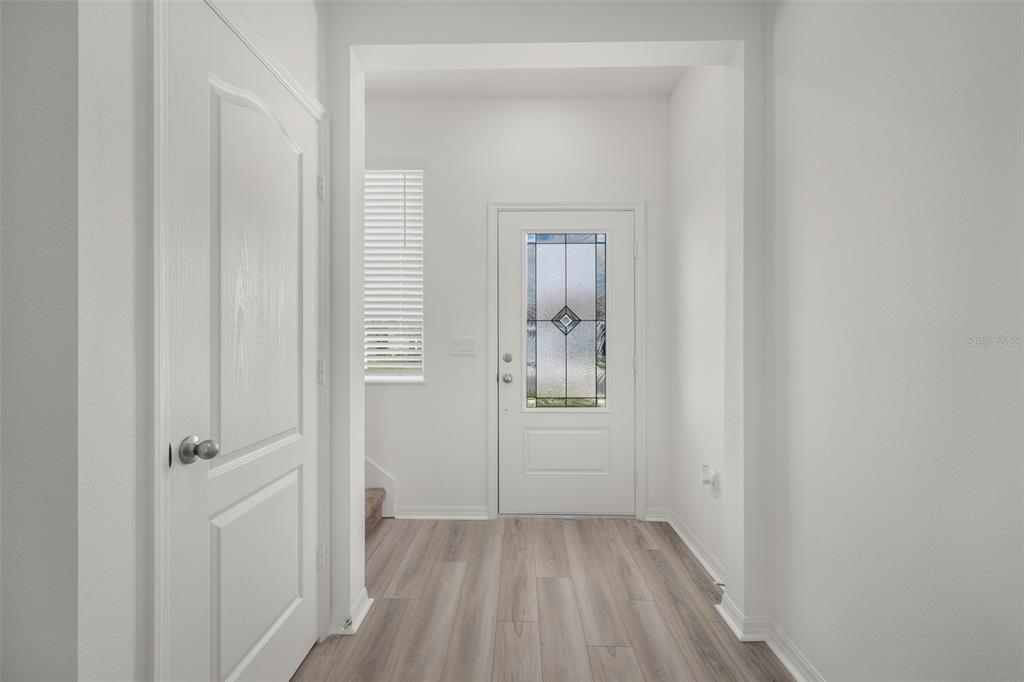 An entryway features light wood-look flooring, white walls, and a front door with glass inlay — 1205 WAHNETA COURT, POINCIANA, FL