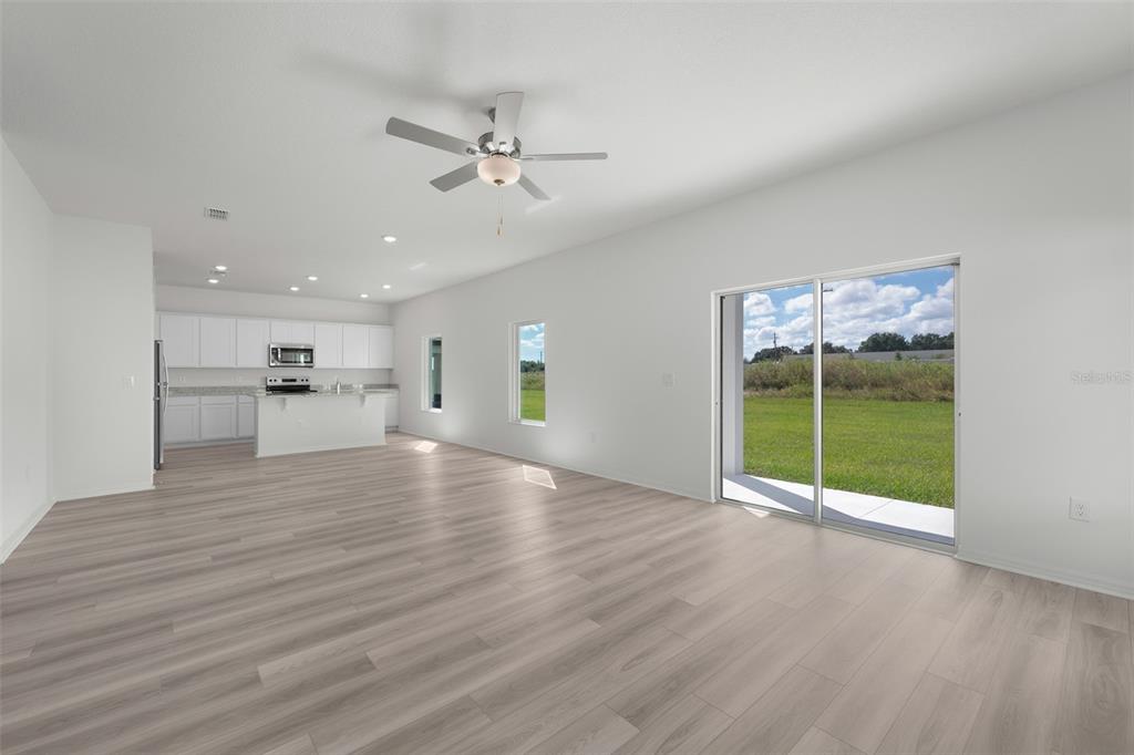 An open-concept living area features light wood-look flooring, a ceiling fan, and sliding glass doors — 1205 WAHNETA COURT, POINCIANA, FL