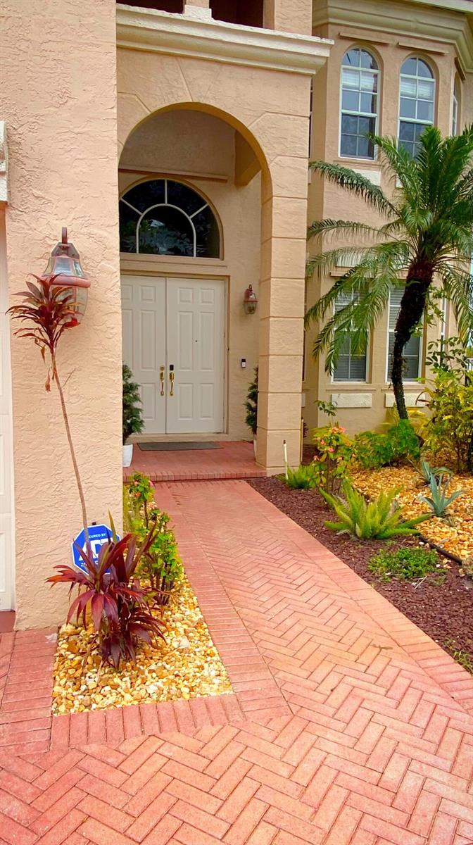 A beige house exterior features a brick walkway leading to a double-door arched entryway — 6489 Marbletree Lane, Lake Worth FL 33467, LAKE WORTH, FL