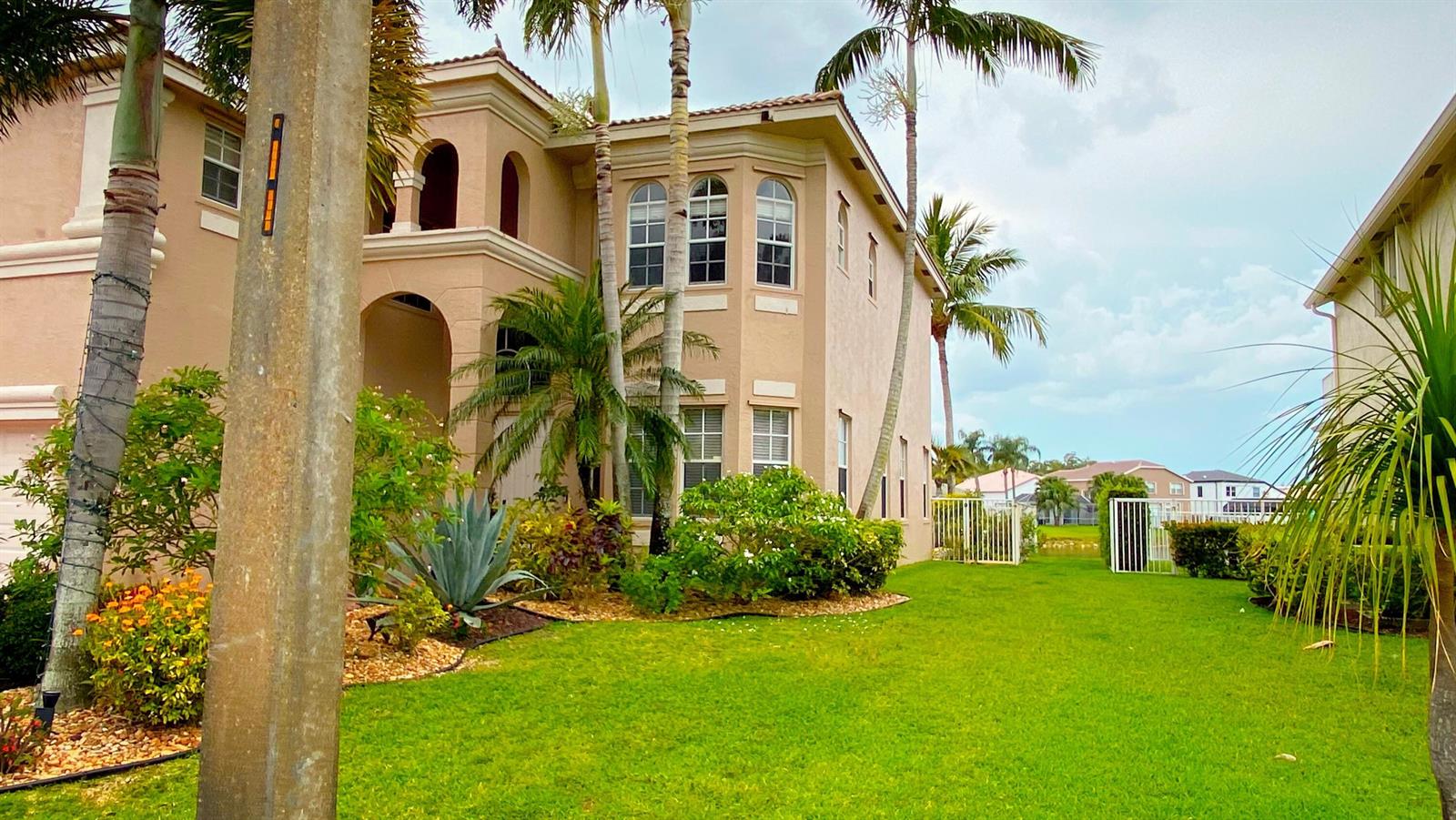 A two-story tan stucco house with arched windows and palm trees in a grassy yard — 6489 Marbletree Lane, Lake Worth FL 33467, LAKE WORTH, FL