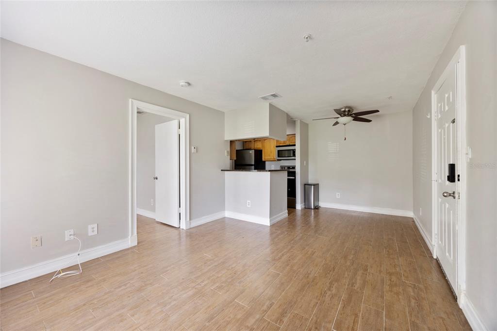 An open-concept living area features light wood-look tile flooring, a ceiling fan, and a kitchen — 241 AFTON SQUARE UNIT 103, ALTAMONTE SPRINGS, FL