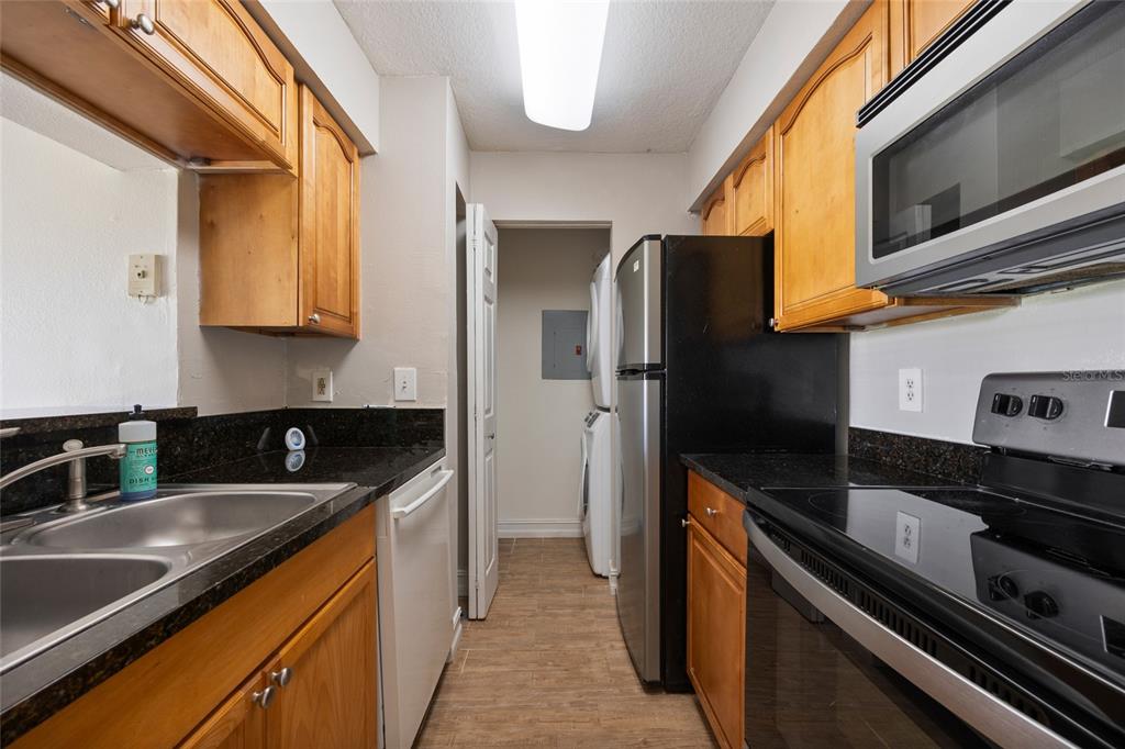 A galley kitchen features wood cabinets, black countertops, stainless steel appliances, and a laundry closet — 241 AFTON SQUARE UNIT 103, ALTAMONTE SPRINGS, FL