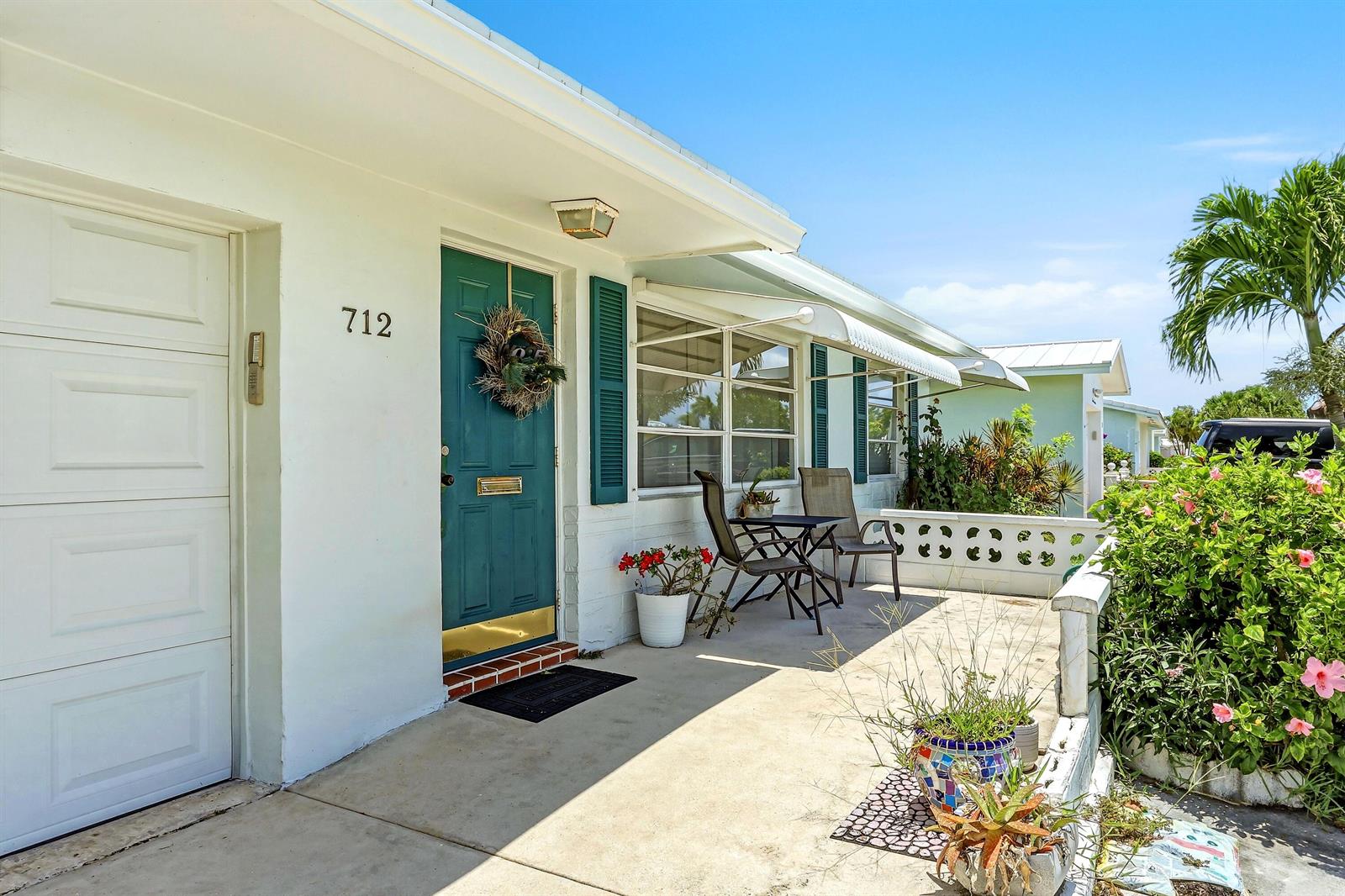 A white house exterior features a teal front door, a concrete porch, and a small table — 712 SW 18th Street, Boynton Beach FL 33426, BOYNTON BEACH, FL